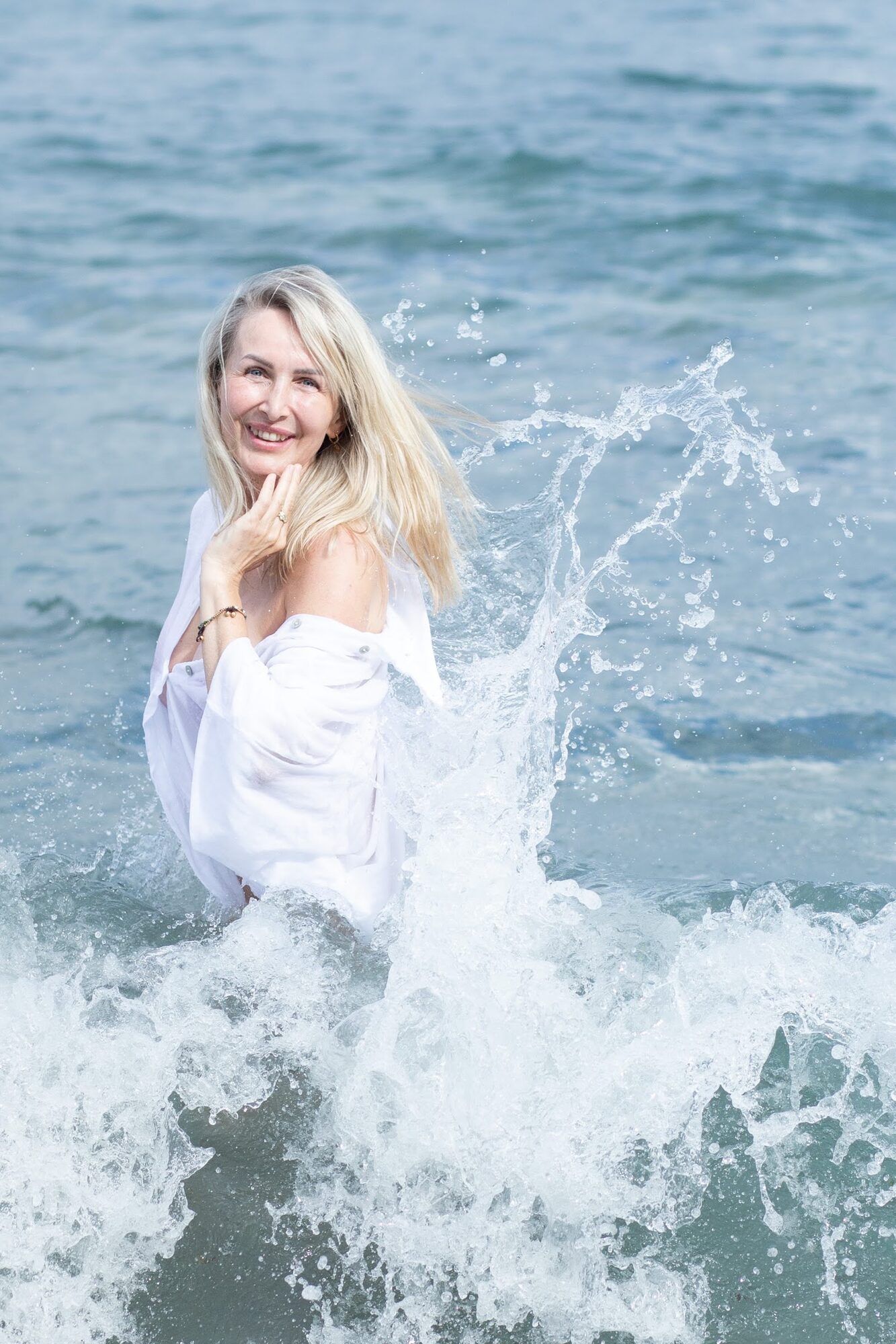 Blondynka w bieli śmieje się, gdy fala rozbija się wokół niej