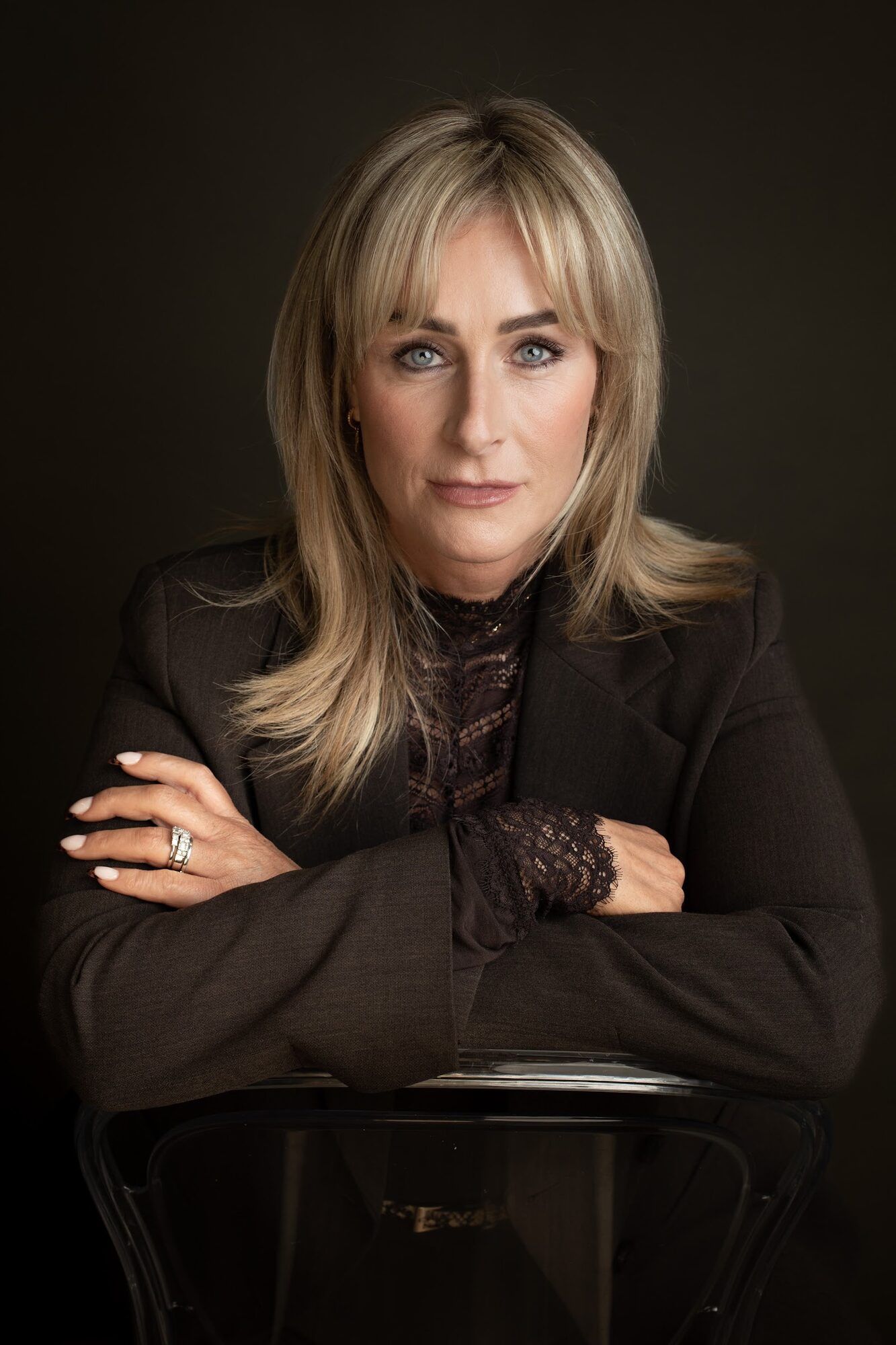 The same woman leaning on the back of a chair, dark backdrop