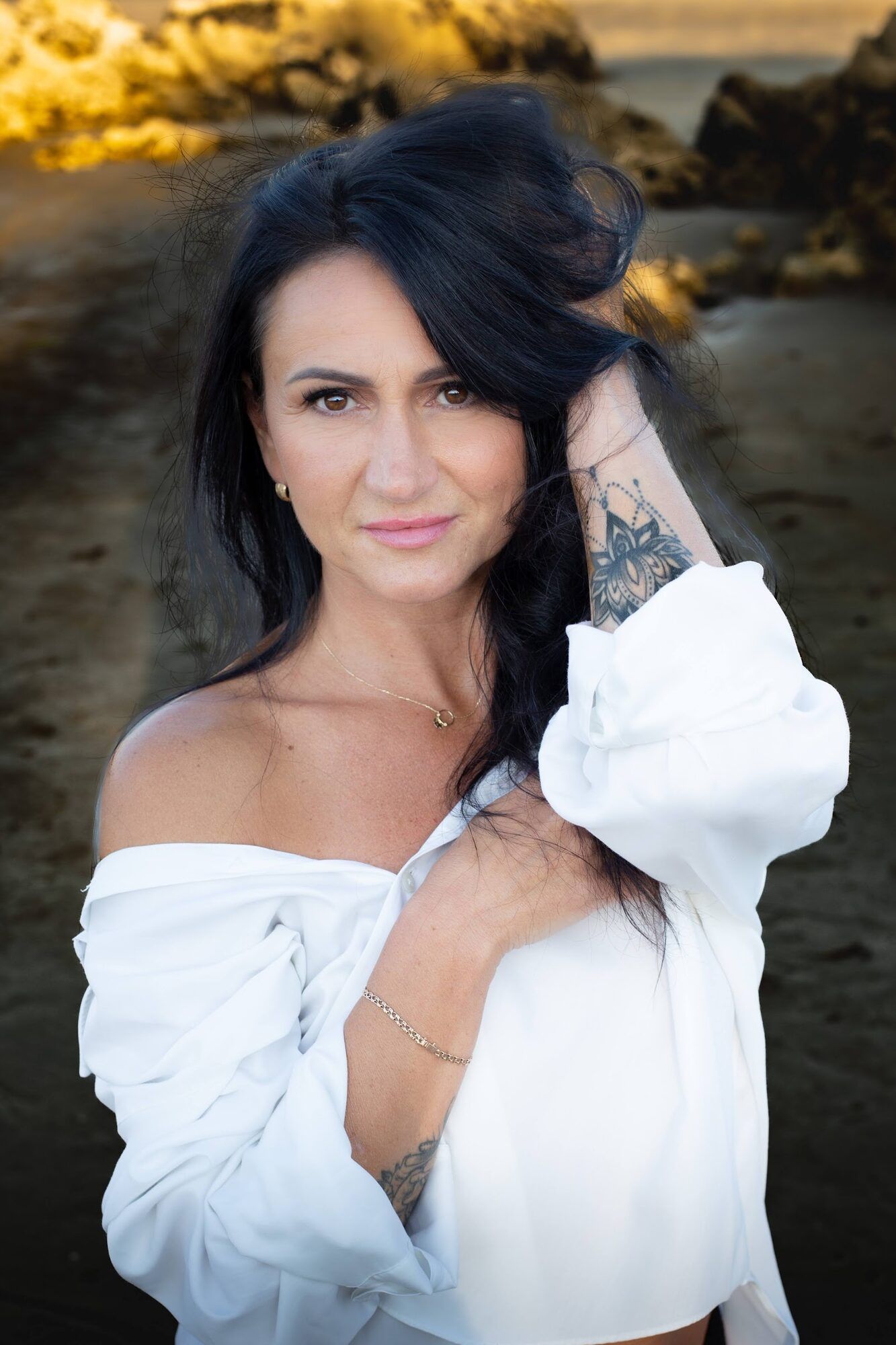 Dark-haired woman in a white shirt on the rocks at sunset