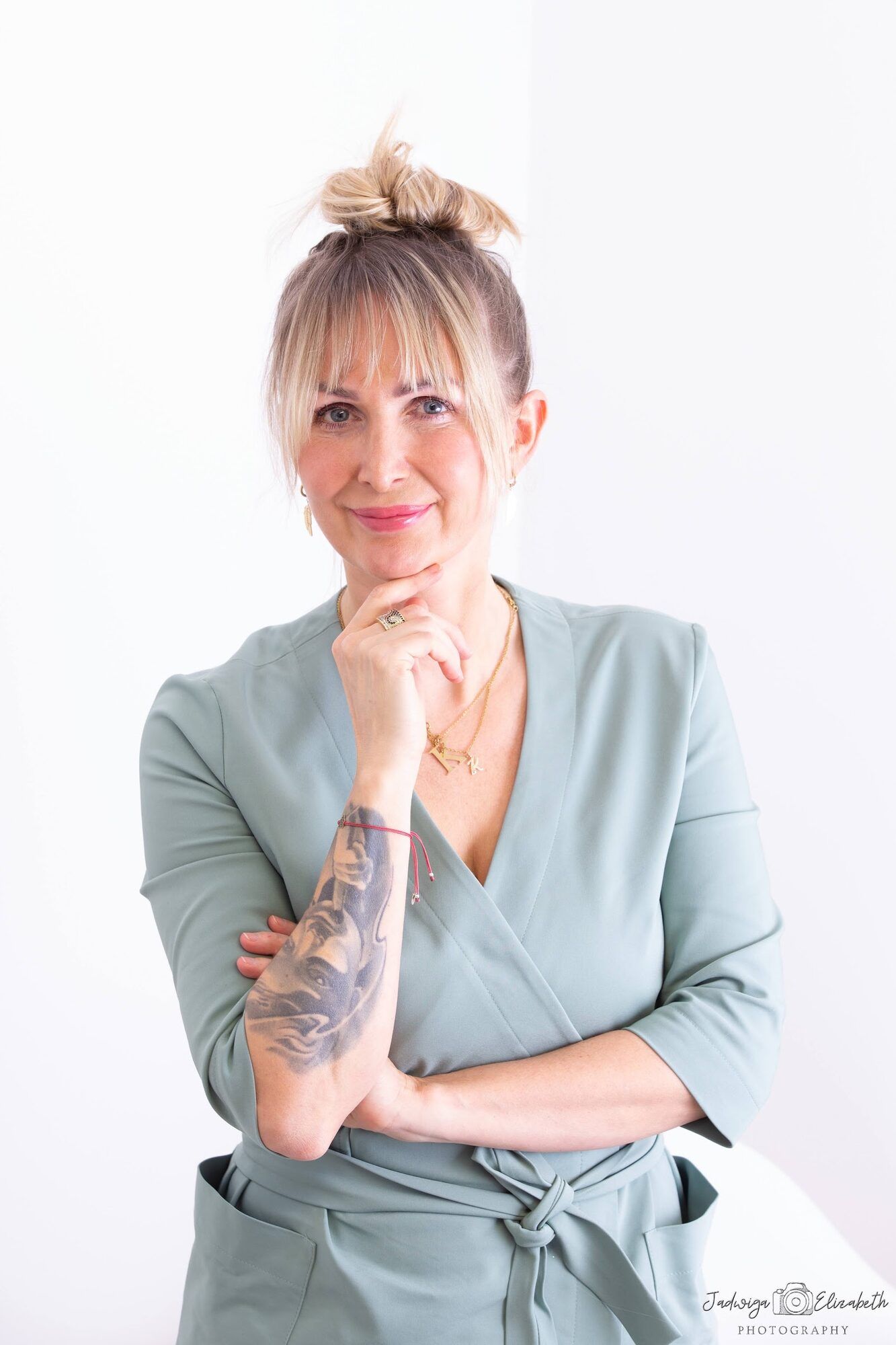 Woman in sage scrubs with a tattooed arm, hand at her chin